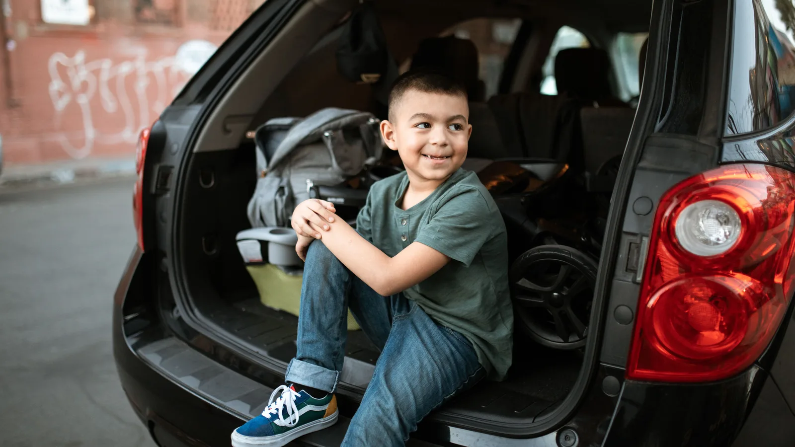 A child sitting beside luggage in the open boot of a family SUV