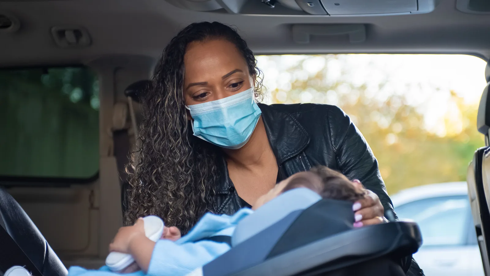 A parent securing a baby into a rearward-facing infant car seat in the back of a car