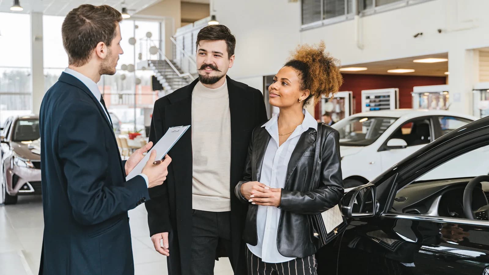 A salesperson showing a car to a couple on a dealership showroom floor